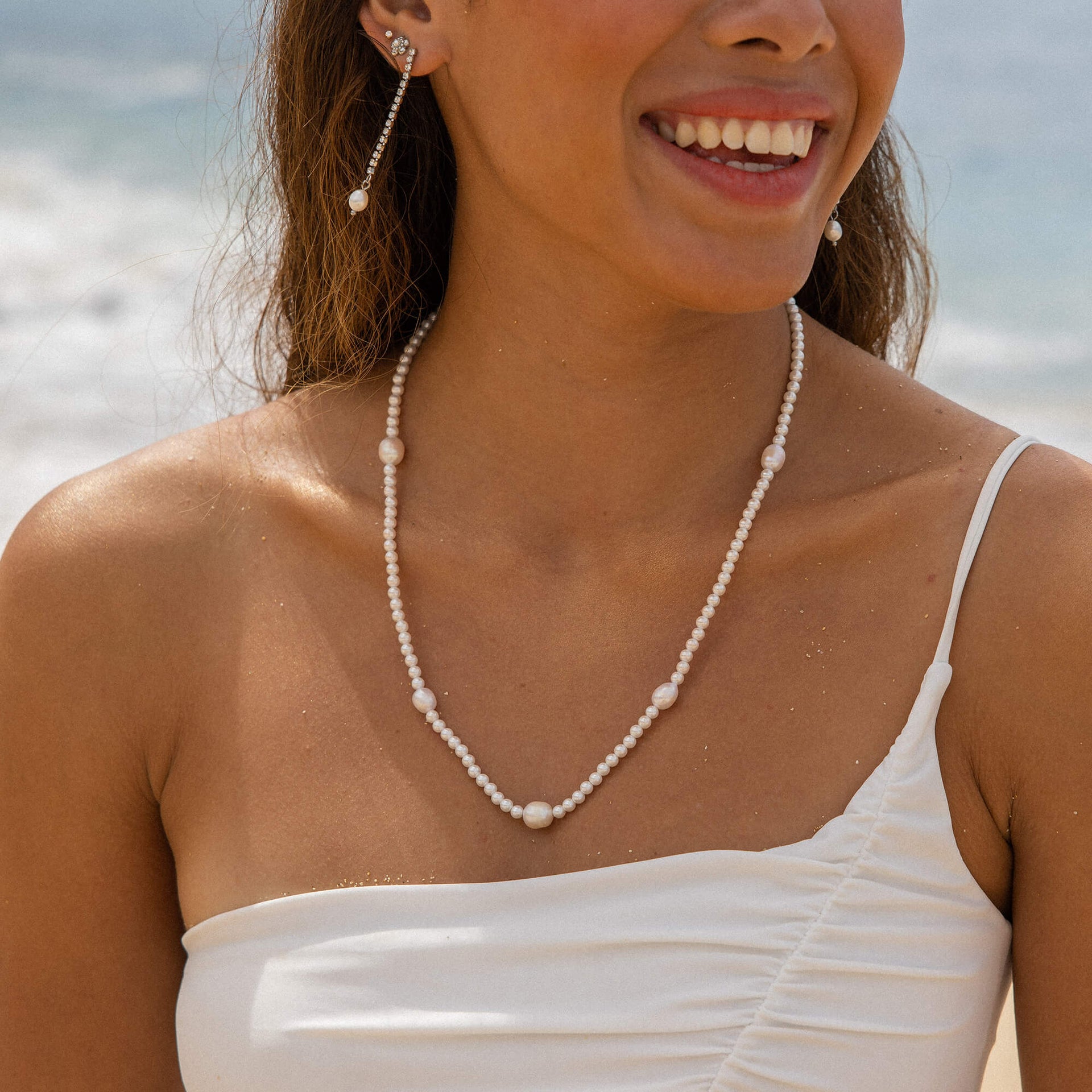 Shimmering Pearl Ohrringe mit Perlen und Strassteinchen in Gold, getragen am Strand – PURELEI Eleganz und Insel-Spirit.