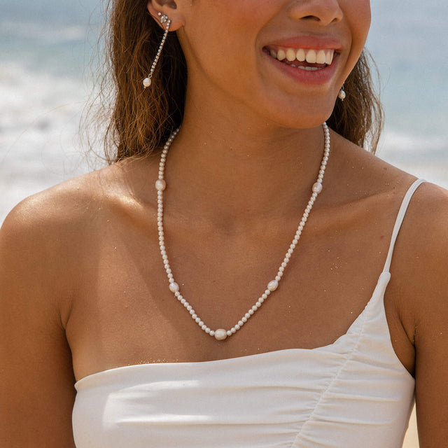 Shimmering Pearl Ohrringe mit Perlen und Strassteinchen in Gold, getragen am Strand – PURELEI Eleganz und Insel-Spirit.