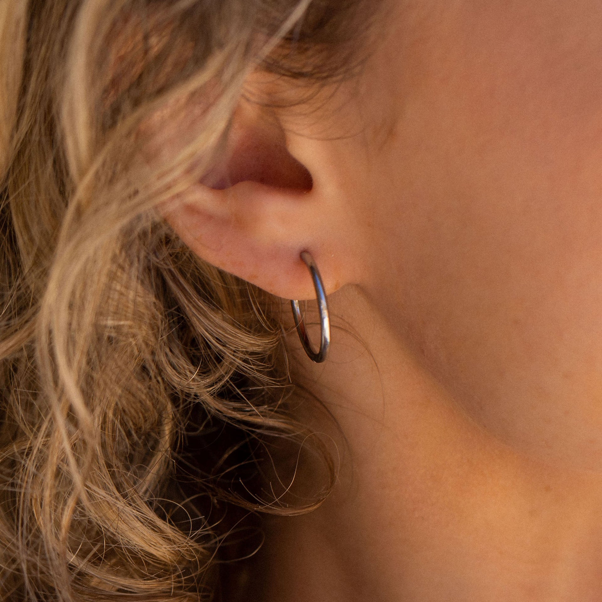 Schlichte, silberne Creolen von PURELEI am Ohr, elegant und zeitlos.