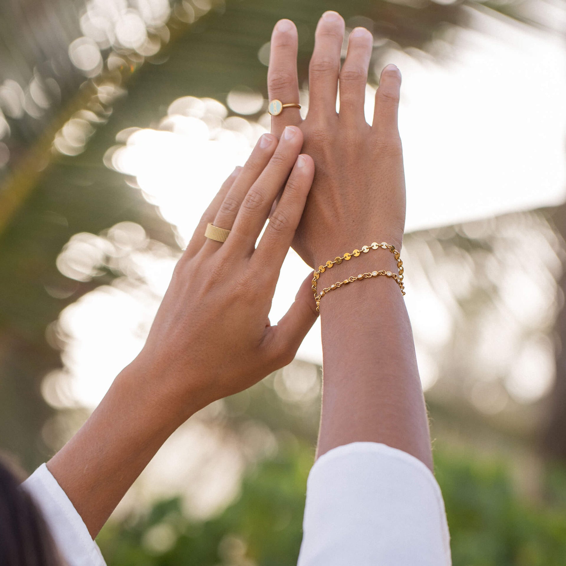 Zarte goldene Armbänder und Ringe von PURELEI, elegant und feminin in tropischer Atmosphäre.