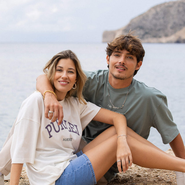 Zwei Personen am Strand, die PURELEI Schmuck tragen, entspannte, tropische Stimmung.