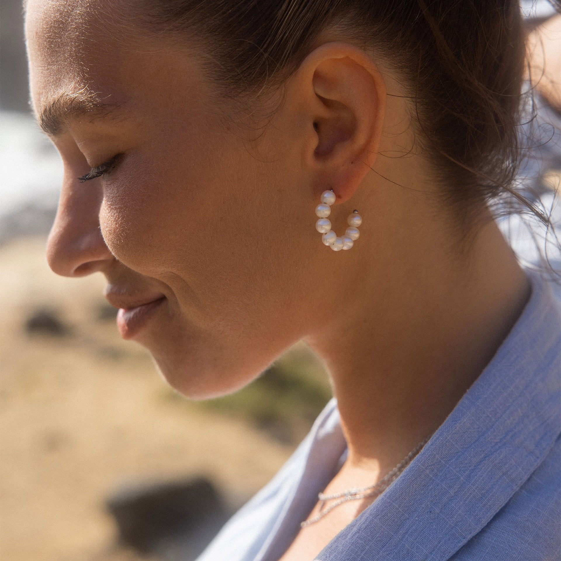 PURELEI Aina Ohrringe mit goldenen Creolen und Perlen, getragen in sanftem Sonnenlicht am Strand.