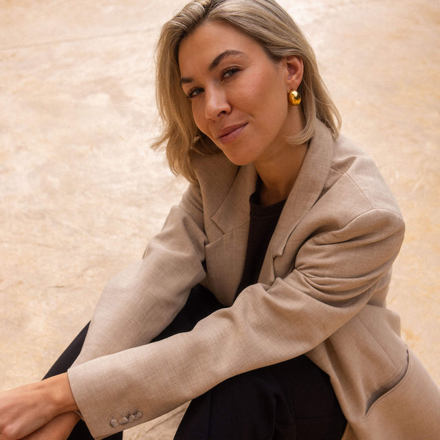 Elegante, goldene Creolen von PURELEI, getragen mit einem beigen Blazer, strahlen zeitlose Schönheit aus.