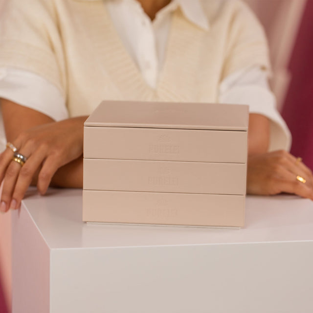 Drei elegante, rosa PURELEI Schmuckboxen auf einem weißen Tisch, umgeben von warmem Licht.