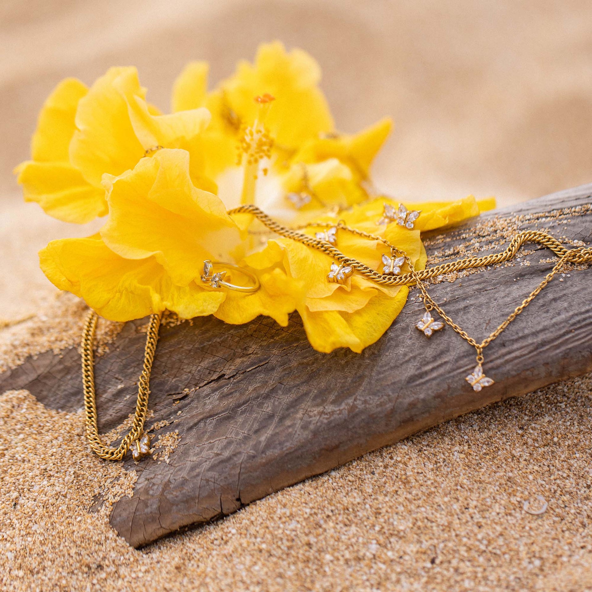 Goldene Schmuckstücke mit Schmetterlingen auf gelber Blüte, PURELEI inspiriert.